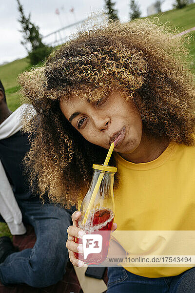 Young woman drinking lemonade by friend in park