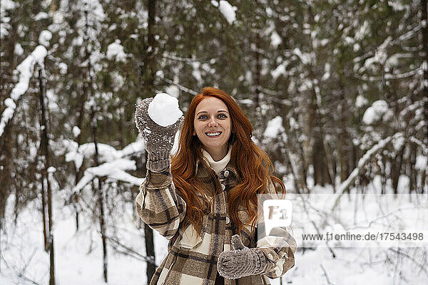 Smiling woman playing with snowball in winter forest