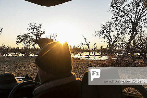 A driver in a jeep looking out at the sunrise.