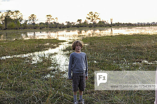 A boy standing alone in an inland delta landscape at sunset.
