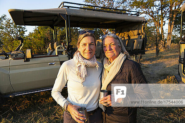 An adult woman and her mother standing side by side  by a jeep at sundown.