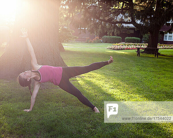 Woman balancing on side in yoga pose in park.