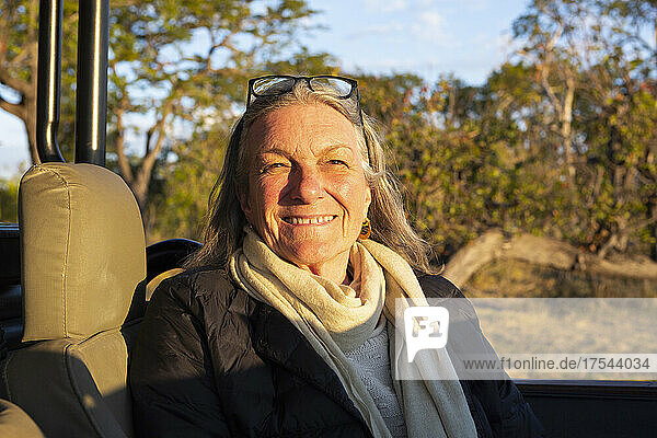 A smiling senior woman seated in a jeep at sunset  smiling.