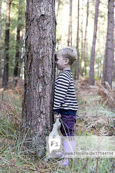 Boy (18-23 months) playing hide and seek in forest