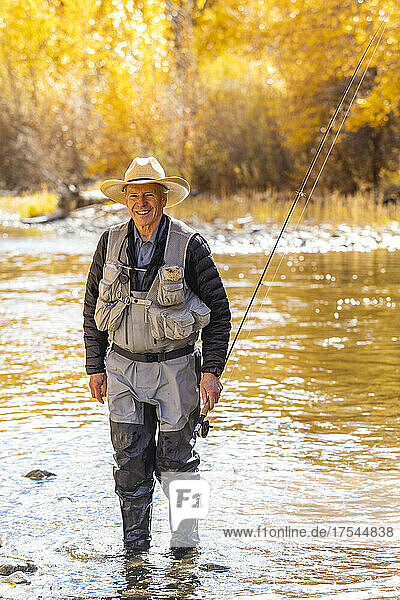 USA  Idaho  Bellevue  Portrait of smiling senior man fly fishing in Big Wood River in Autumn