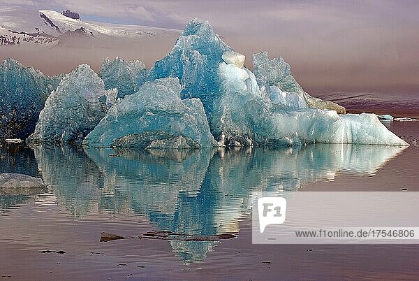 Blauer Eisberg spiegelt sich im Wasser  Berge ragen aus dem Nebel  Jökulsarlon  Gletscherlagune  Skandinavien  Island  Europa
