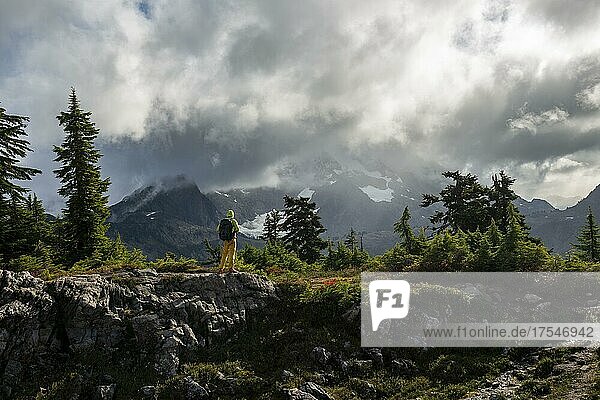 Hiker in front of cloudy Mt. Shuksan with snow and glacier  dramatic cloudy sky  Mt. Baker-Snoqualmie National Forest  Washington  USA  North America