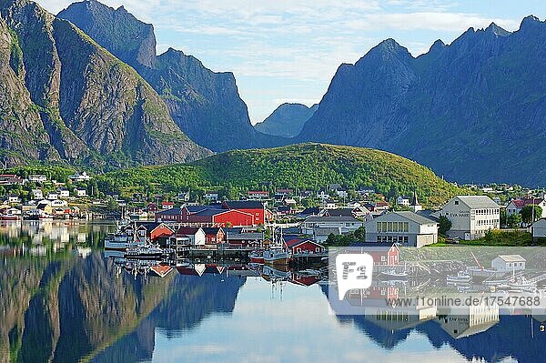 Ortsansicht  Reinefjord mit Bergen und roten Holzhäusern  Häuser und Berge spiegeln sich im Fjord  Reine  Moskenesöy  Lofoten  Nordland  Norwegen  Europa