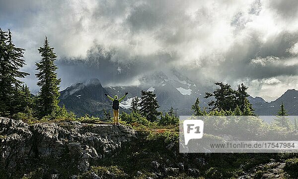 Wanderer streckt die Arme in die Luft  vor wolkenverhangenem Mt. Shuksan mit Schnee und Gletscher  dramatischer Wolkenhimmel  Mt. Baker-Snoqualmie National Forest  Washington  USA  Nordamerika