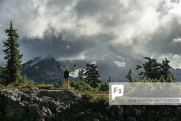 Wanderer streckt die Arme in die Luft  vor wolkenverhangenem Mt. Shuksan mit Schnee und Gletscher  dramatischer Wolkenhimmel  Mt. Baker-Snoqualmie National Forest  Washington  USA  Nordamerika
