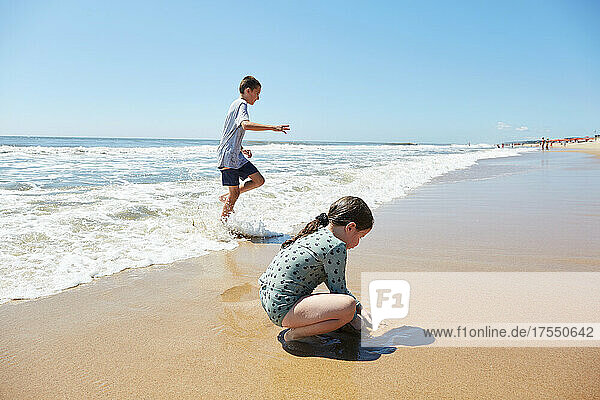 Boy (8-9) and girl (2-3) playing on beach 