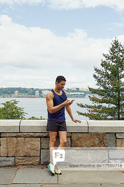 USA  New York  New York City  Man in sports clothing looking at smart phone at wall in park