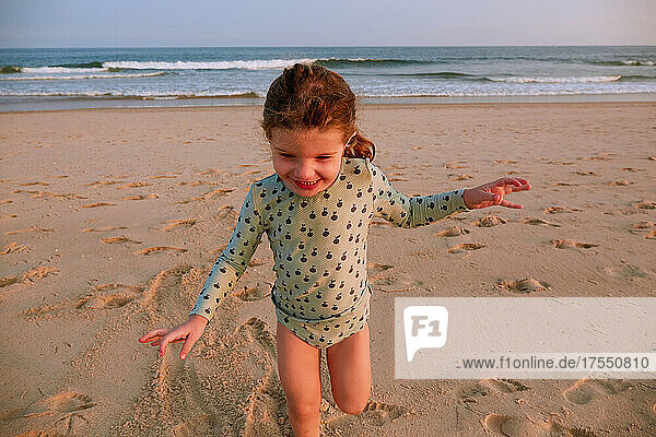 Smiling girl (2-3) playing on beach at sunset