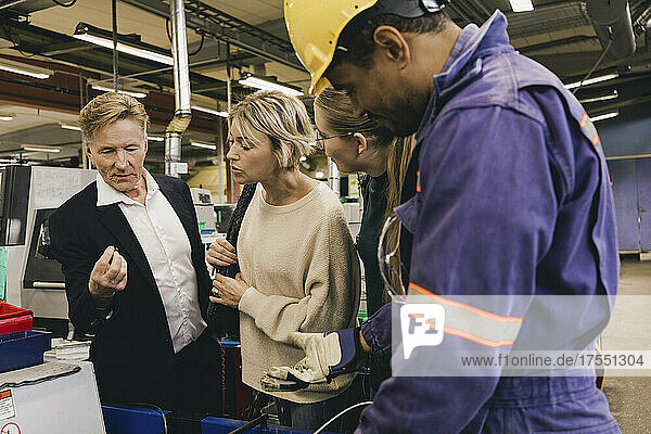 Male worker in protective workwear discussing with businessman and family in industry