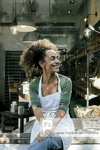 Lächelnde Unternehmerin schaut weg  während sie vor einer Bäckerei sitzt