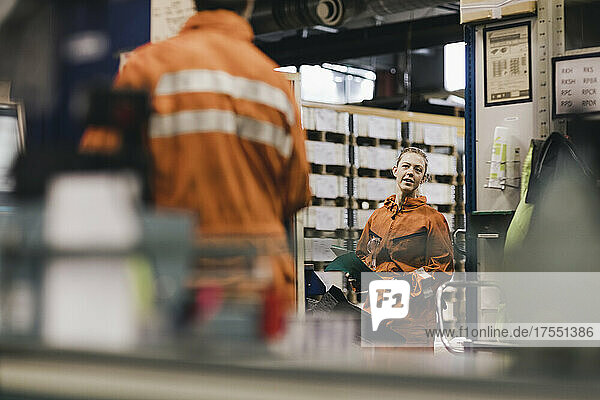 Weiblicher Arbeiter in Uniform diskutiert mit einem männlichen Kollegen in einer Fabrik