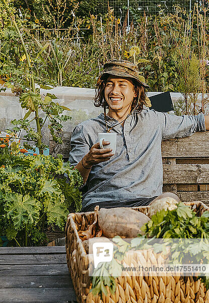 Lächelnder Landwirt mit Kaffeetasse auf einer Bank auf einem Bauernhof