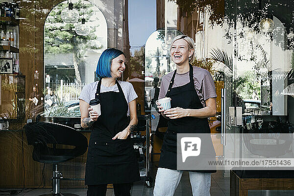 Fröhliche Mitarbeiterin mit Kaffeetasse  die vor einem Friseursalon steht