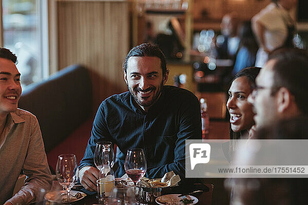Happy multiracial male and female friends having wine in restaurant