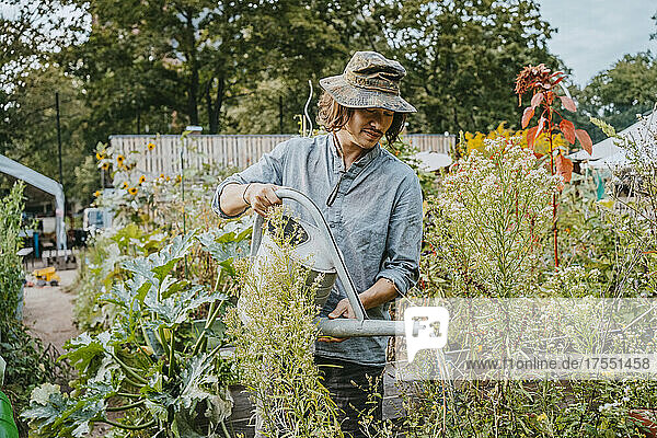 Mann mit Hut bewässert Pflanzen im städtischen Garten