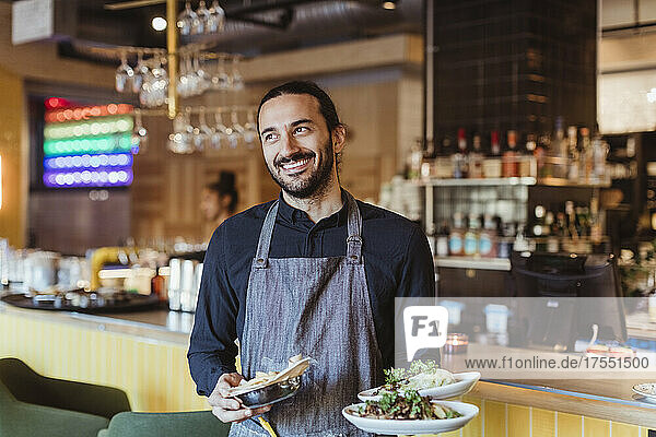 Happy male waiter with food looking away in bar