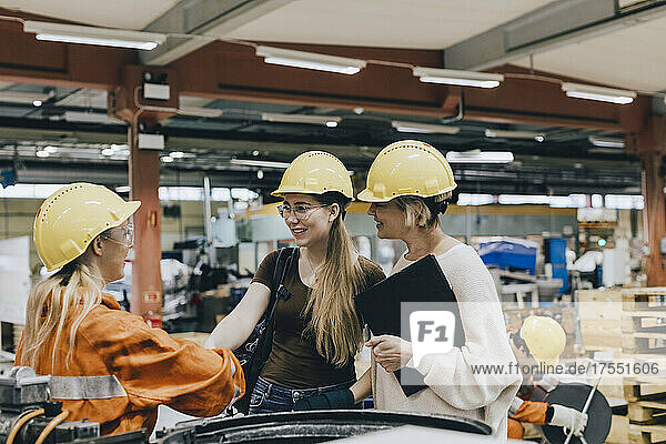 Lächelnde Geschäftsfrauen im Gespräch mit einer Arbeiterin in einer Fabrik