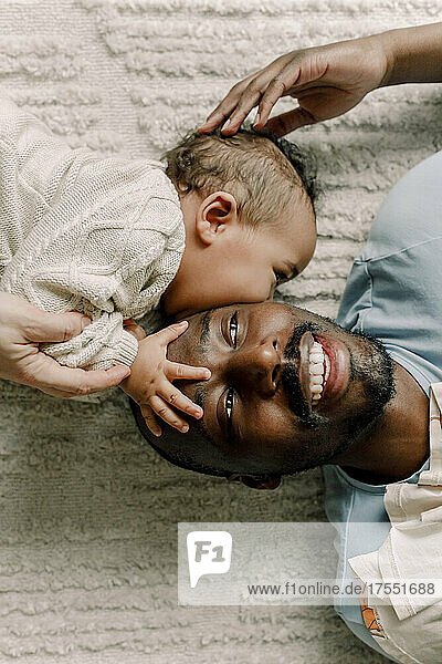 Männliches Kleinkind küsst Vater auf Decke liegend zu Hause