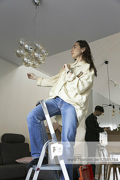 Junge Frau bei der Installation eines Kronleuchters während eines Umzugs zu Hause
