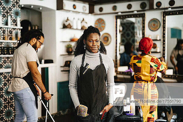 Portrait of confident young female hairdresser with hands in pockets at barber shop
