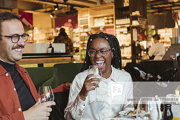 Glückliche Frau trinkt Wein mit einem männlichen Freund während einer Party im Restaurant