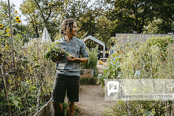 Lächelnder männlicher Bauer mit Gemüse im Gemeinschaftsgarten