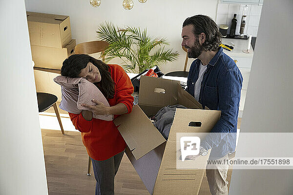 Frau stützt sich auf ein Kissen  während ein Mann eine Kiste in ein neues Haus trägt
