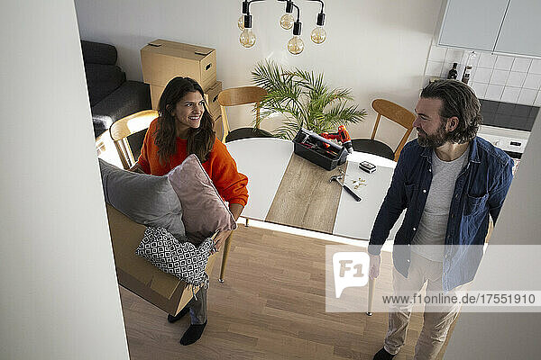 Smiling woman carrying box while talking with man in living room