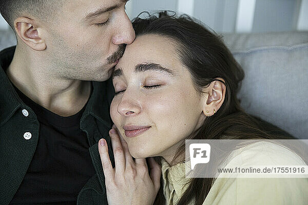 Zärtlicher Mann küsst die Stirn seiner Freundin im Schlafzimmer zu Hause