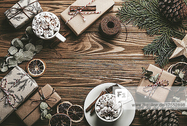 Christmas decorated background with wrapped presents  fir tree branch  marshmallow cacao cups on wooden table. Happy Xmas wrapping gift boxes top view with copy space template