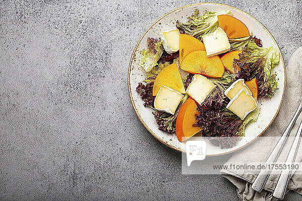 Persimmon salad with brie cheese and fresh salad leaves