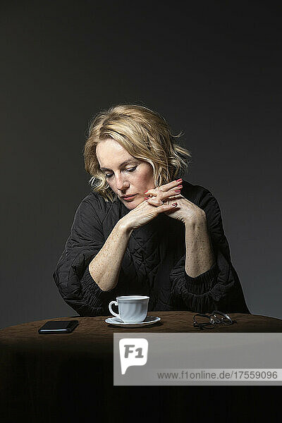 Blonde Frau mit Kaffee schaut auf ihr Smartphone