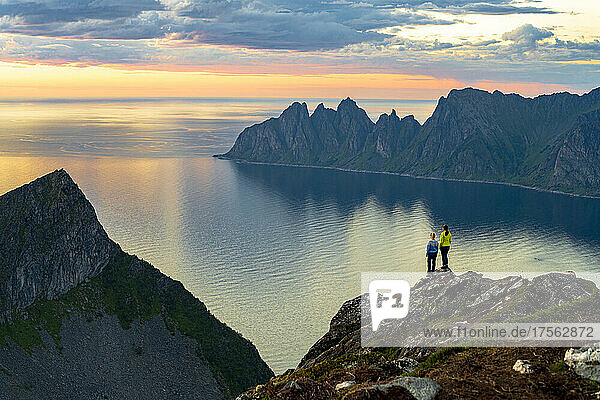 Two young women watching sunset standing on mountain top  Senja island  Troms county  Norway  Scandinavia  Europe
