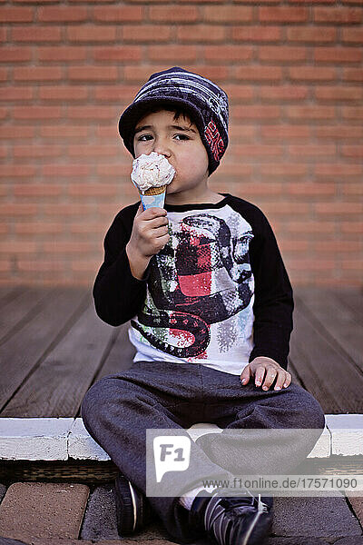 Boy eating ice cream in front of a brick wall.