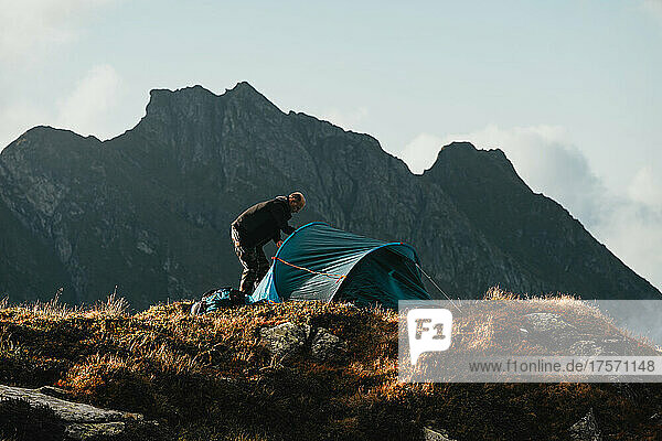 Man setting tent at campsite with mountains in the background