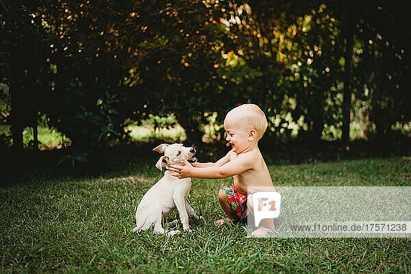 Adorable smiling toddler about to hug a white puppy in summer