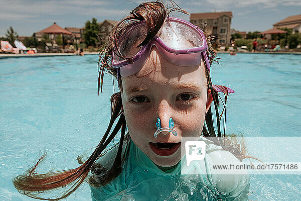Goofy young girl in pool with goggles on forehead