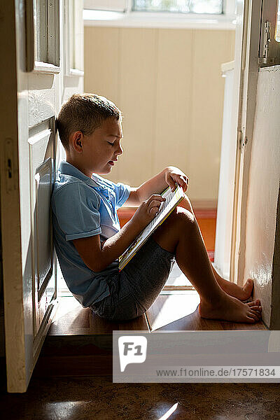 The boy is sitting on the threshold and reading a book