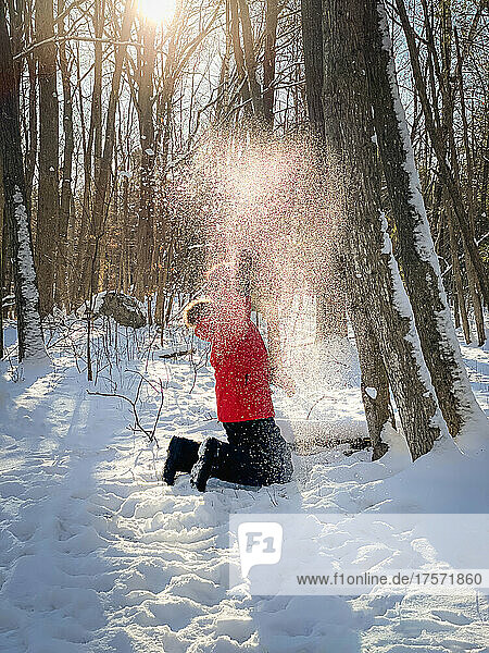 Young boy in red winter coat playing in the snow in the woods.