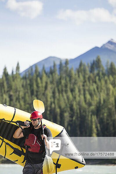 Scenic image of man carrying yellow raft (packraft) in wilderness.