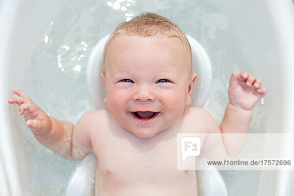 Cheerful baby 6 months old bathes in a baby bath