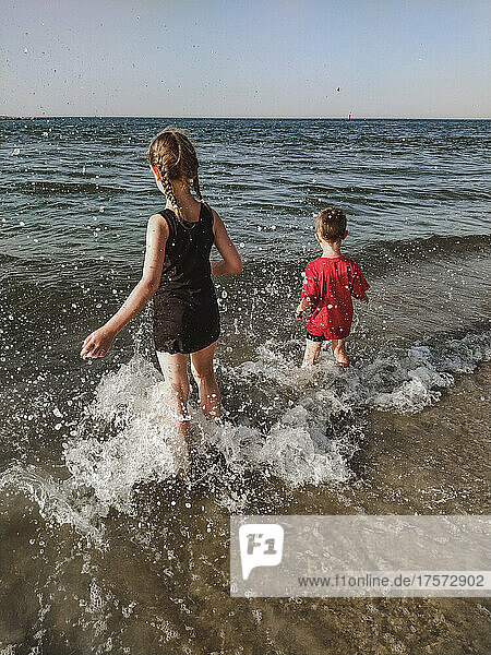 Two children have fun in the splashes of the sea on the shore