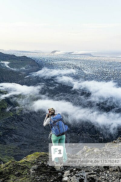 Wanderin blickt über spektakuläre Landschaft  Nebel an Klippen und Gletscher Myrdalsjökull  Pakgil  Island  Europa