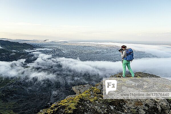 Hiker photographs spectacular landscape  fog on cliffs and glacier Myrdalsjökull  Pakgil  Iceland  Europe