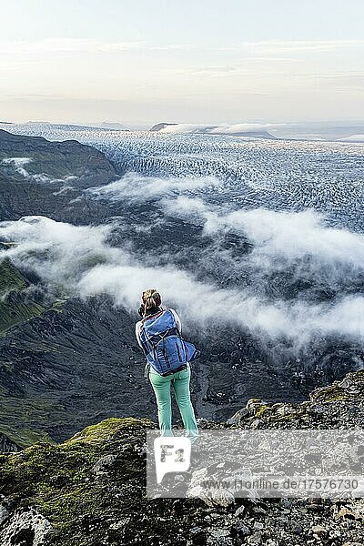 Hiker looks over spectacular landscape  mist on cliffs and glacier Myrdalsjökull  Pakgil  Iceland  Europe